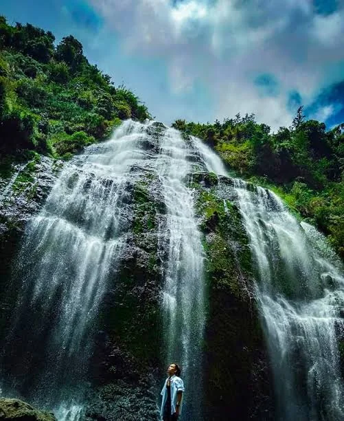 A tall waterfall descending a green mountainside in Bauko